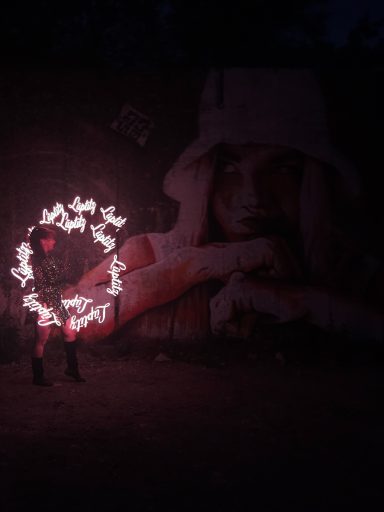 Lichtershow Sommerfest Lüptitz: Person mit Leuchtstäben, umgeben von einer Wandmalerei bei Nacht.